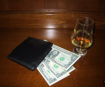Predator Wallet by R. Paul Wilson on top of bills and next to alcohol on wooden table